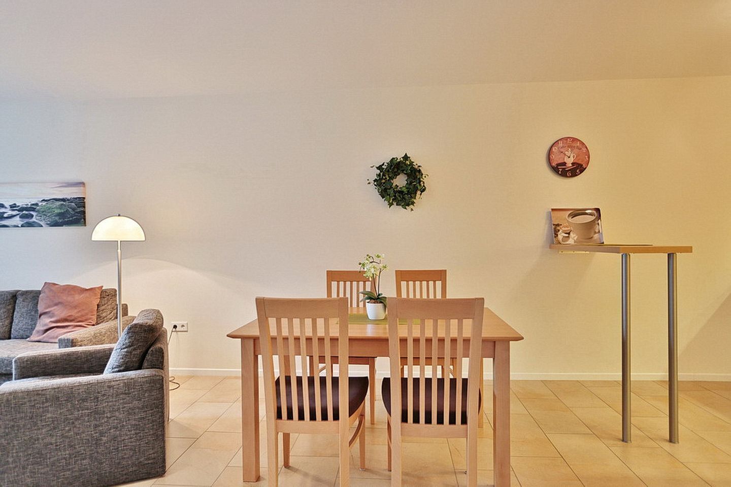 Un coin repas avec une table et des chaises en bois, une petite plante en pot et une étagère fixée au mur sur laquelle se trouve un plateau.