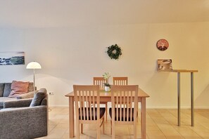 Un comedor con una mesa y sillas de madera, una pequeña planta en maceta y una repisa en la pared con una bandeja.