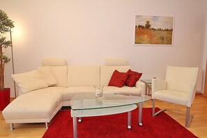 A modern living room with a beige sectional sofa, a glass coffee table, a red rug, and a painting on the wall.