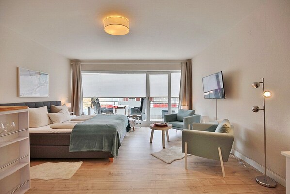 Una habitación de hotel moderna con una cama, dos sillones, un televisor y un ventanal con vistas a la ciudad.
