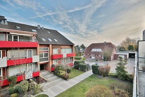 Ein Wohngebäude mit roter und grauer Fassade, mehreren Balkonen und einem gepflegten Garten.