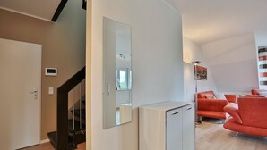 A modern living space with a staircase, a mirrored wall, and a seating area with orange sofas.