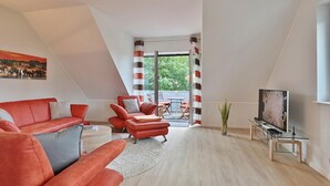 A modern living room with a red sofa, a red armchair, and a glass coffee table. There is a television on a stand and a window with curtains.
