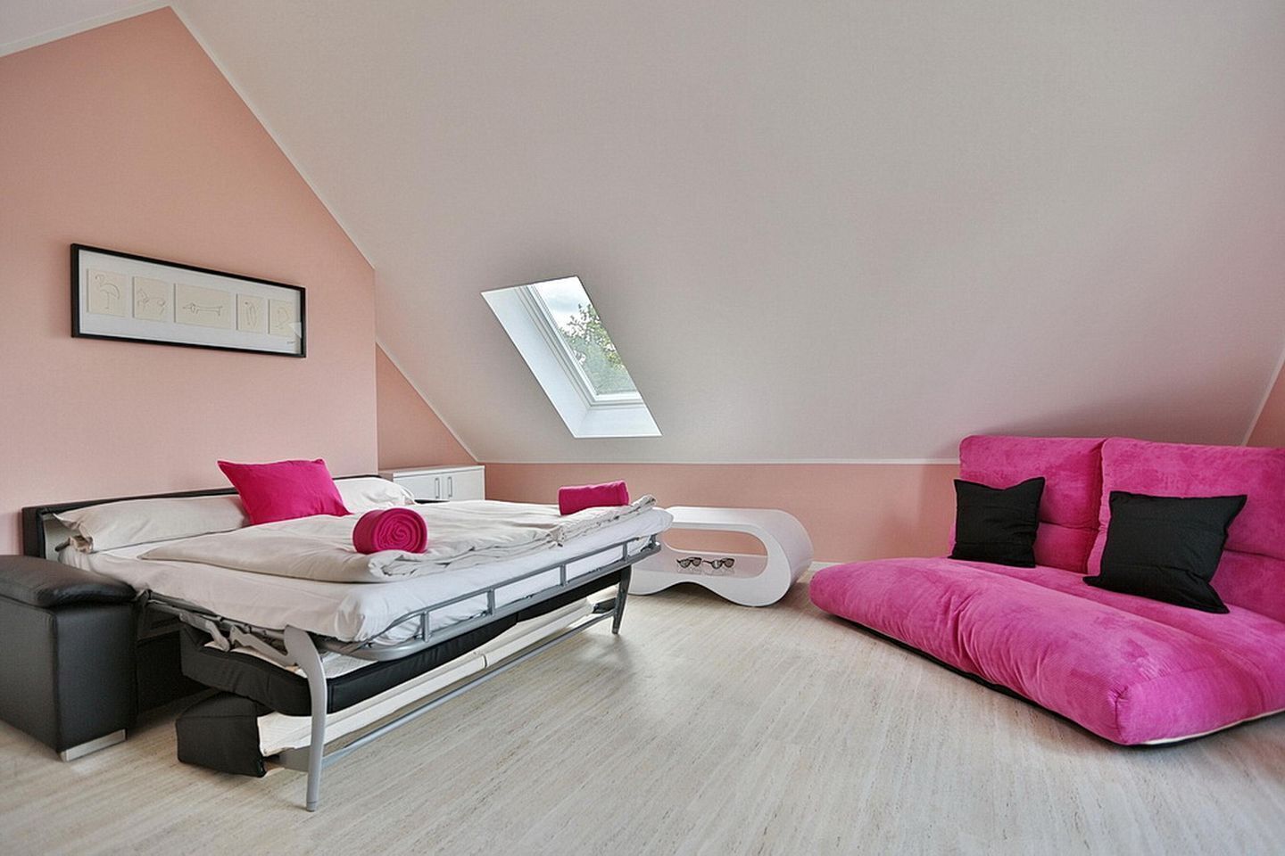A bedroom with a bed, a pink sofa, a small white table, and a skylight.