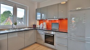 A modern kitchen with grey cabinets, a built-in oven, and a window with a view of houses.