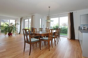 Un comedor con una mesa redonda de madera, sillas, ventanas amplias y una planta en maceta.