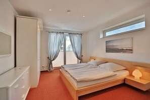 Una habitación de hotel con cama, mesita de noche, armario, ventana con cortinas y un cuadro en la pared.