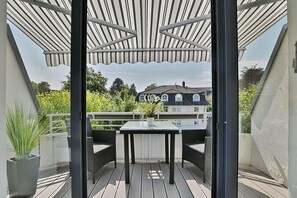 A balcony with a table and chairs, a potted plant, and a view of houses in the background.