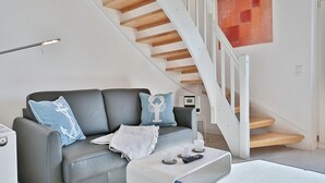 A modern living room with a grey sofa, a coffee table, and a staircase with wooden steps. - Treffert Apartment 38 - House Miramar (Timmendorfer Strand)