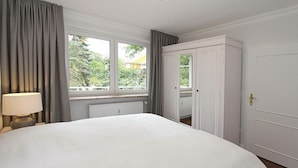 Une chambre d’hôtel avec un grand lit, une fenêtre avec des rideaux, un radiateur et une armoire.