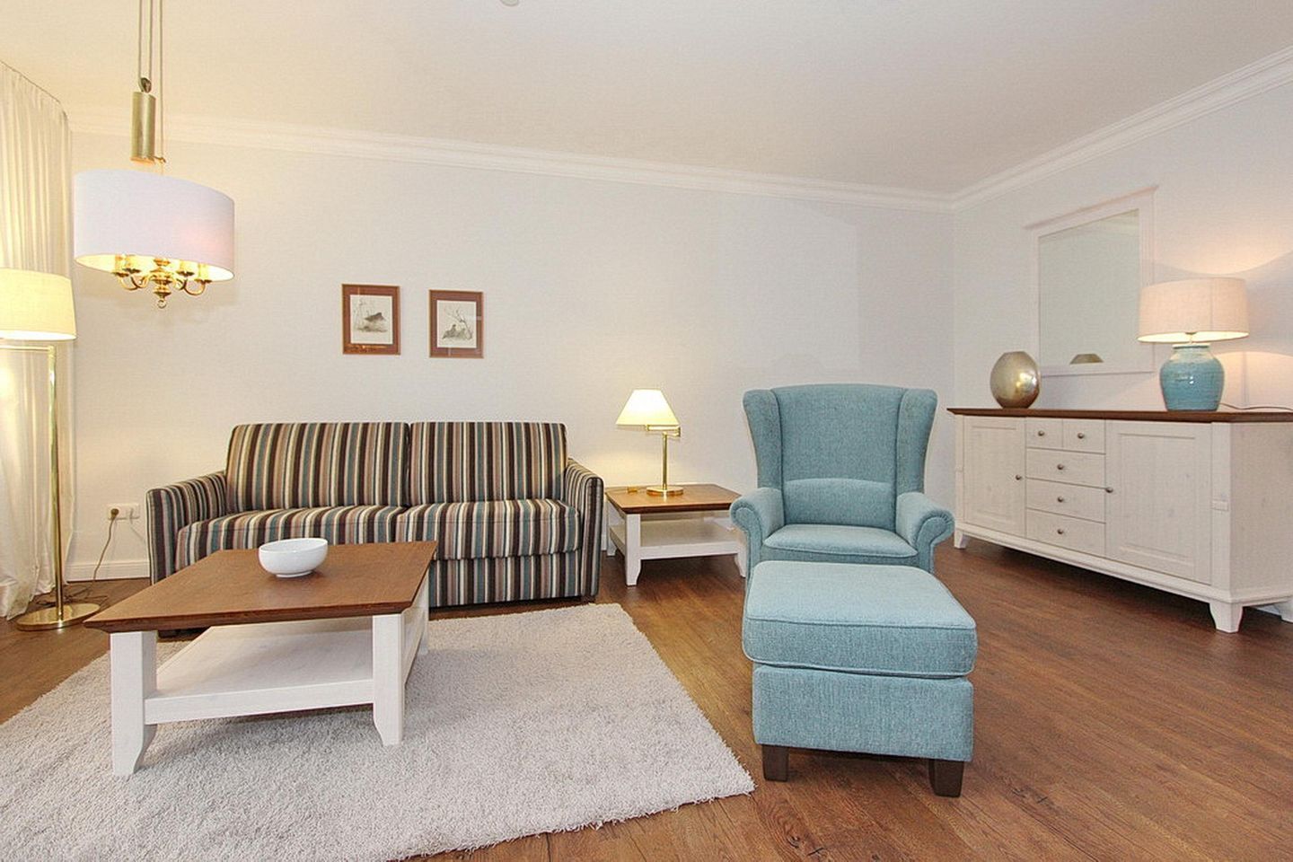 A living room with a striped sofa, a blue armchair, a wooden coffee table, a white side table, and a white cabinet with decorative items.