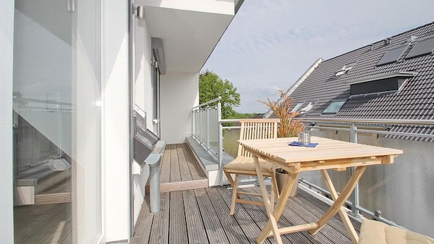 Una terraza de madera con una mesa y sillas, un ventanal de vidrio y vistas a edificios cercanos.