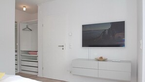 Un dormitorio con una cama, un armario, un televisor montado en la pared y una mesita con un cuenco.
