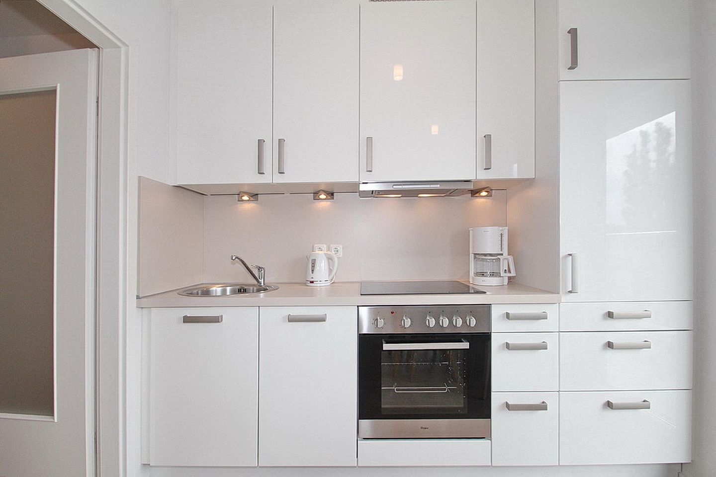 Una cocina moderna con armarios blancos, un lavamanos de acero inoxidable, una cafetera y un horno empotrado.