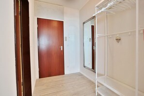 Un couloir avec une porte en bois, un mur blanc et un miroir.