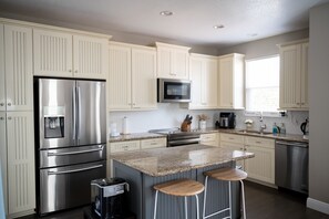 A modern kitchen with stainless steel appliances, a granite countertop, and light-colored cabinetry. - Tran- Quility beach house (Rosemary Beach)