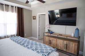 Ein Schlafzimmer mit einem großen Bett, einem an der Wand montierten Fernseher, einem Holzschrank und einer Tür zu einem weiteren Raum.