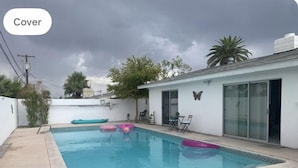 Ein Schwimmbecken mit überdachtem Bereich, eine Terrasse mit Stühlen und einer Schmetterlingsdekoration an der Wand.