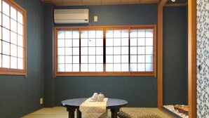 Ein traditioneller japanischer Raum mit Tatami-Boden, einem niedrigen Tisch mit weißem Tuch und vier gemusterten Kissen.