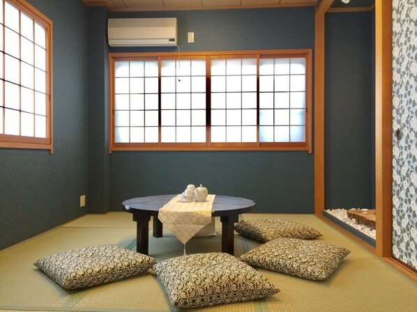 A traditional Japanese room with tatami flooring, a low table with a white tablecloth, and four patterned cushions. - Fuse Private 1 House, 4LDK (東大阪市)