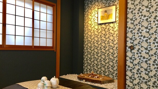 Ein traditioneller japanischer Raum mit Tatami-Boden, einem niedrigen Tisch mit Tee-Set, einem Shoji-Bildschirm und einer Wand mit Kirschblütenmuster.