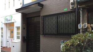 Ein Gebäude mit moderner Fassade, einem großen Fenster mit Rasteroptik und einer kleinen, grünen Schachtel über dem Eingang.