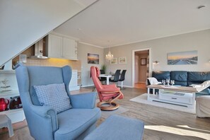 A modern living room with a blue armchair, a red recliner, a sofa, and a dining area with a table and chairs.