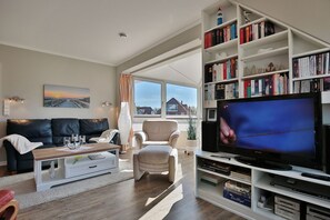 A modern living room with a sofa, armchair, coffee table, and a bookshelf filled with books.