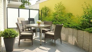 Eine Terrasse im Freien mit Tisch und Stühlen, umgeben von Pflanzen und einer gelben Wand.