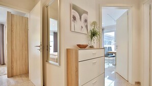 Ein moderner Flur mit einer Holztür, einer weißen Kommode mit Schubladen, einem Spiegel und einem gerahmten Kunstwerk darüber.