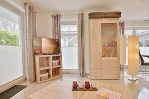 Un soggiorno moderno con TV a schermo piatto, mobili contenitori in legno, una porta in vetro e un'area pranzo con tavolo e sedie.