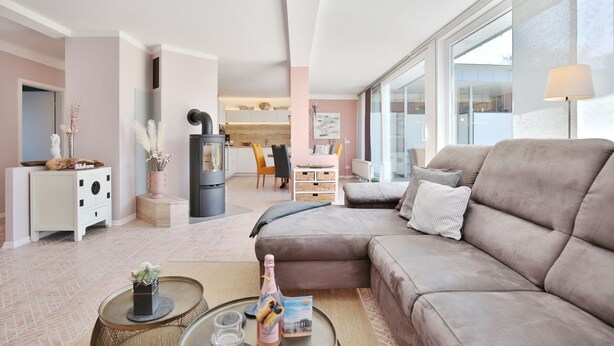 Ein modernes Wohnzimmer mit einer Couch, einem Couchtisch und einem Kamin. Im Hintergrund ist eine Küchenzeile mit einem Esstisch und Stühlen zu sehen.