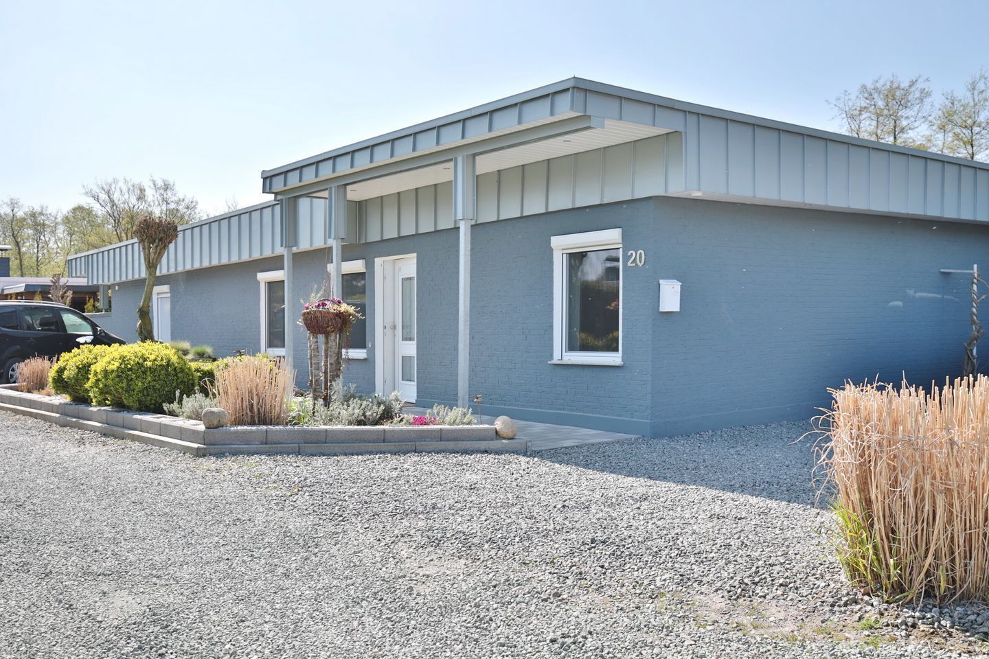 A modern building with a grey exterior, a number '20' sign, and a gravel driveway.