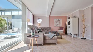 Ein modernes Wohnzimmer mit großem Fenster, einem grauen Sofa, einem kleinen runden Tisch und einer Zierpflanze.