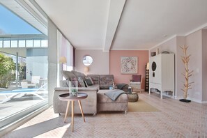Un soggiorno moderno con un'ampia finestra, un divano grigio, un tavolino rotondo e una pianta decorativa.