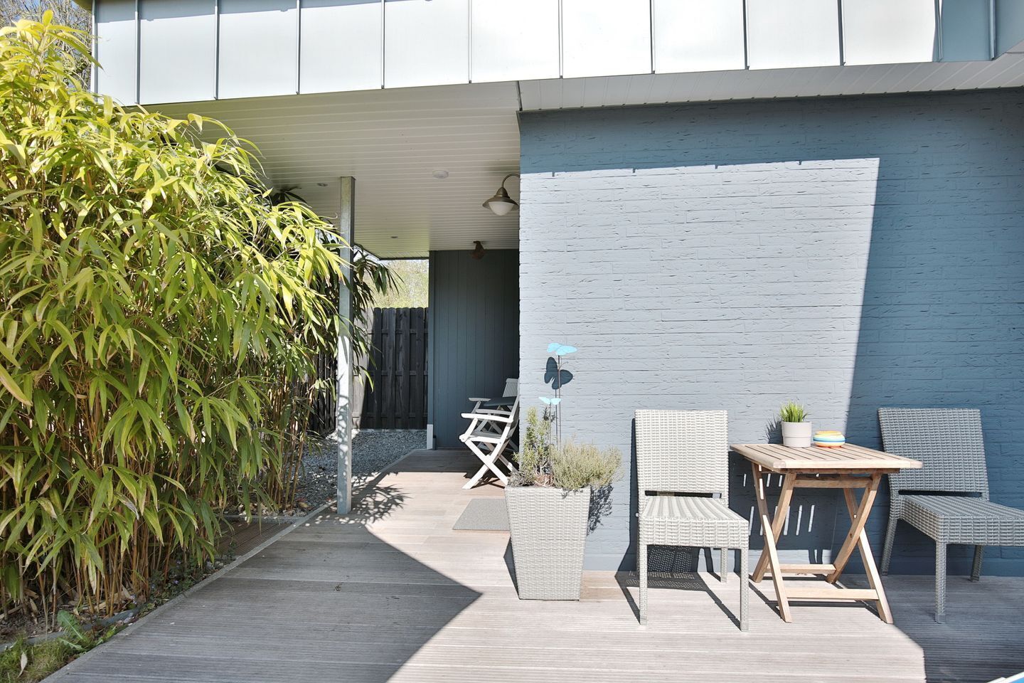 A modern outdoor patio with a wooden deck, wicker furniture, and a blue wall.