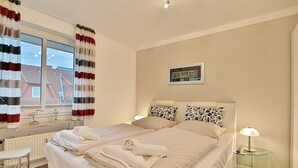 Habitación de hotel con cama, dos mesitas de noche, ventana con cortinas, radiador y un pequeño cuadro en la pared.
