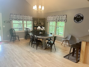 A dining area with a round table, chairs, a chandelier, and large windows with patterned valances. - Private Lakefront, Dog Friendly w/HOT TUB Home!SWIM/SKI/RELAX! (Central Lake)