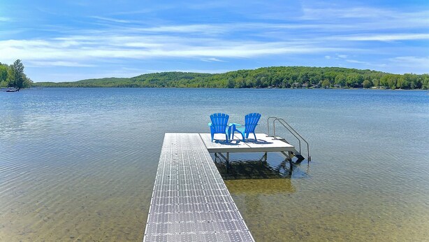 A dock with a clear view of a lake, surrounded by greenery and a clear sky.