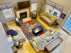 A living room with a fireplace, sofas, a coffee table, and a large window. - Private Lakefront, Dog Friendly w/HOT TUB Home!SWIM/SKI/RELAX! (Central Lake)