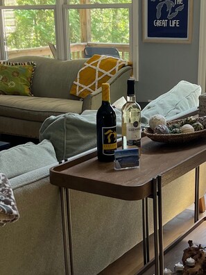 A living room with a sofa, a coffee table with bottles, a framed picture, and a window with a view of trees. - Private Lakefront, Dog Friendly w/HOT TUB Home!SWIM/SKI/RELAX! (Central Lake)