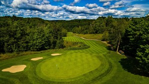A golf course with sand bunkers, a flagstick, and a clear sky.
