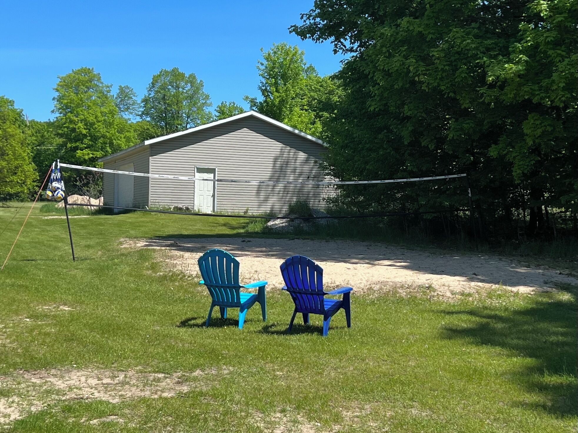 A grassy yard with two blue chairs, a volleyball net, and a shed.