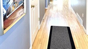 A hallway with a wooden floor, a black rug, a door, and a poster of a boat on the water.
