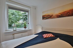 Et soveværelse med seng, et vindue med udsigt til grønne områder, en radiator og et billede på væggen.