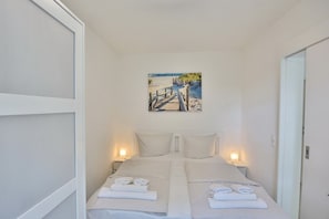 A hotel room with a bed, two bedside tables, a painting of a beach scene, and a door.