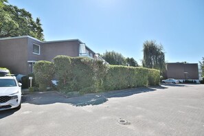 A residential street with a row of houses, a hedge, and parked cars.