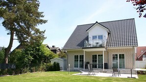 A two-story house with a tiled roof, a covered patio with outdoor furniture, and a well-maintained lawn.