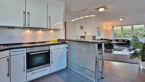 A modern kitchen with white cabinets, a built-in oven, and a dining area with a black sofa and a dining table.