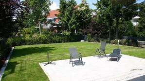 A patio area with four lounge chairs and a small table, surrounded by a well-maintained lawn and trees.